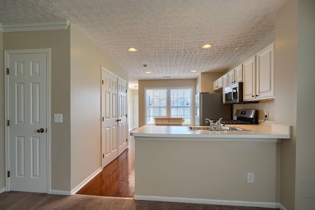 kitchen with appliances with stainless steel finishes, a peninsula, light countertops, baseboards, and a sink