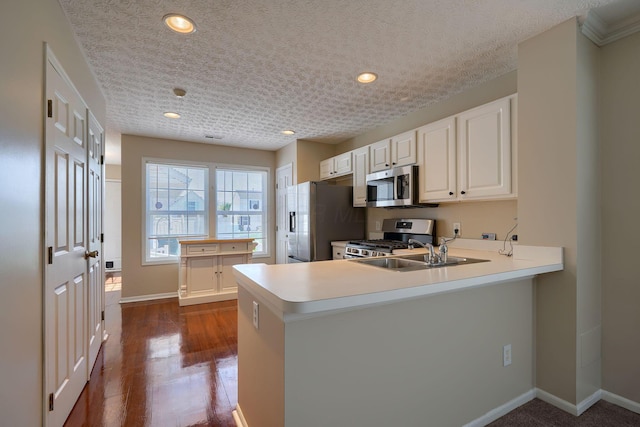 kitchen with appliances with stainless steel finishes, a sink, a peninsula, light countertops, and baseboards
