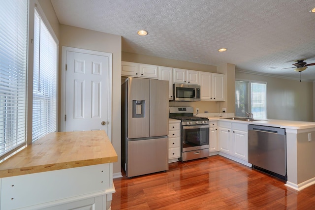 kitchen with appliances with stainless steel finishes, a textured ceiling, a peninsula, wood finished floors, and white cabinets