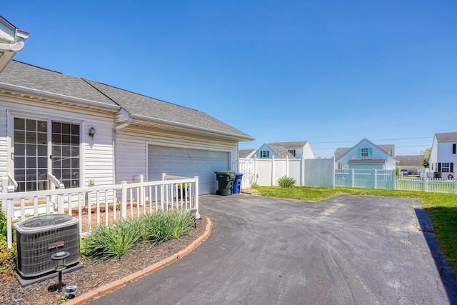 exterior space featuring asphalt driveway, roof with shingles, central AC, and fence