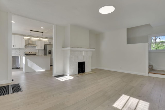 unfurnished living room featuring stairway, visible vents, light wood finished floors, and a brick fireplace
