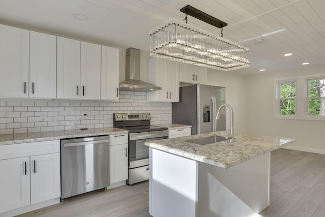 kitchen featuring appliances with stainless steel finishes, white cabinets, a sink, light wood-type flooring, and wall chimney exhaust hood