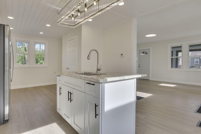 kitchen with light wood-style flooring, freestanding refrigerator, white cabinets, a sink, and baseboards