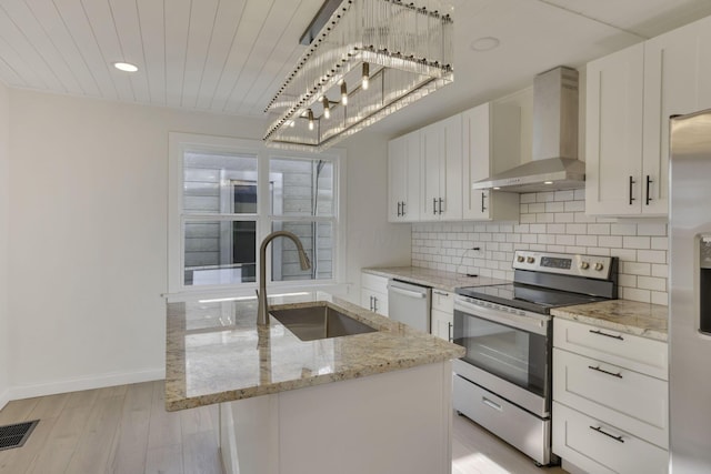 kitchen with wall chimney range hood, white cabinetry, a sink, appliances with stainless steel finishes, and light wood-style floors