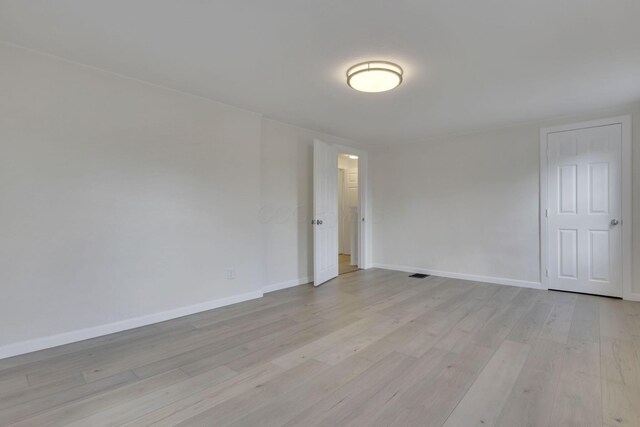 empty room with light wood-style floors, visible vents, and baseboards