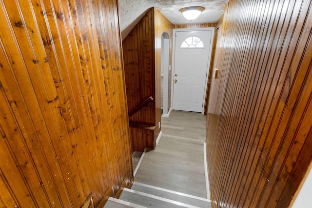stairway featuring wooden walls, arched walkways, and wood finished floors