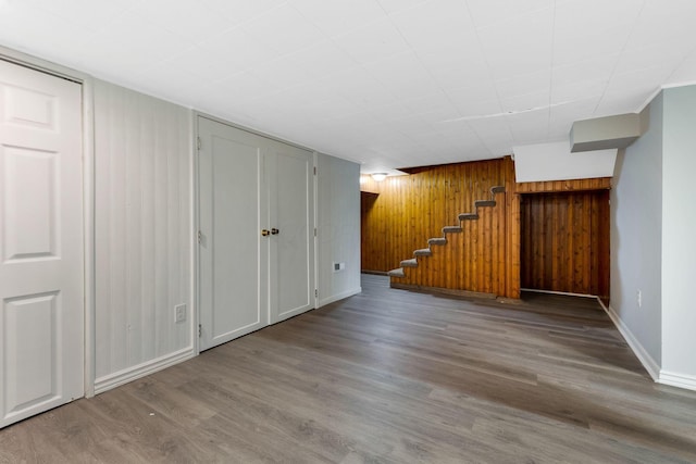 finished below grade area featuring baseboards, wood walls, wood finished floors, and stairway