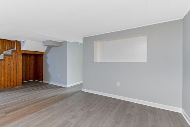 unfurnished living room with wooden walls, baseboards, and wood finished floors