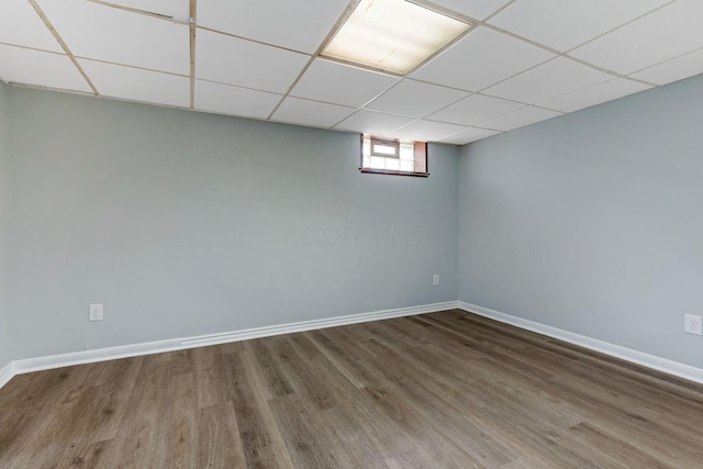 basement featuring baseboards, a drop ceiling, and wood finished floors