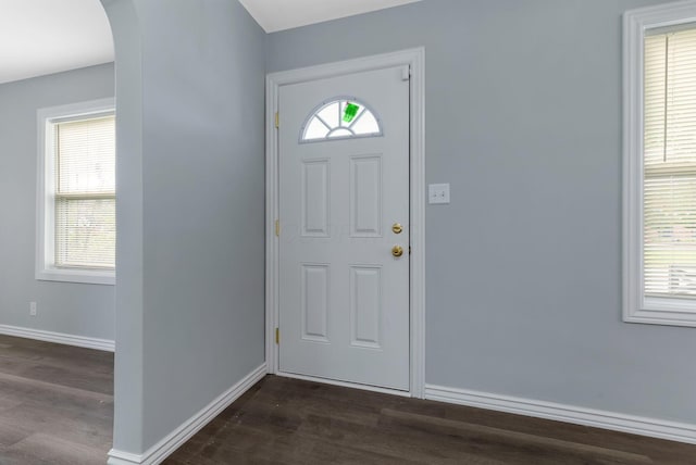 foyer with dark wood-type flooring, arched walkways, and baseboards