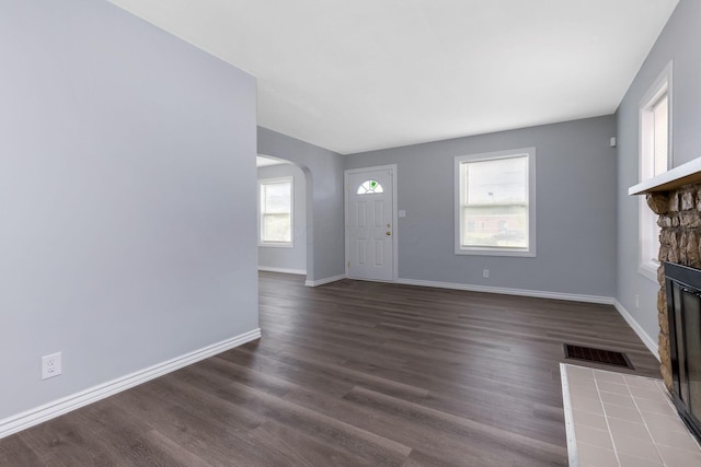 unfurnished living room with visible vents, a fireplace, baseboards, arched walkways, and dark wood finished floors
