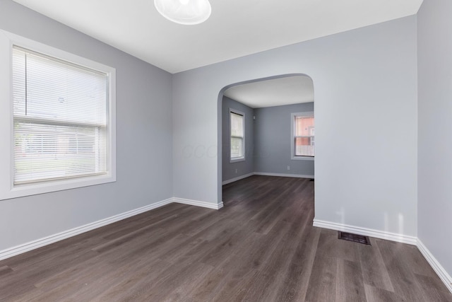 spare room featuring baseboards, arched walkways, wood finished floors, and visible vents