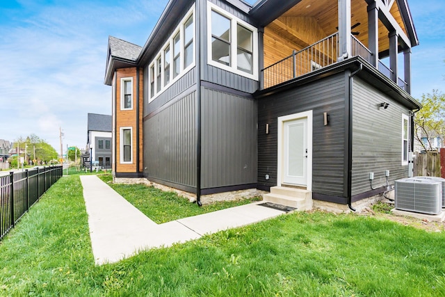 rear view of property featuring fence, entry steps, central AC unit, a balcony, and a yard