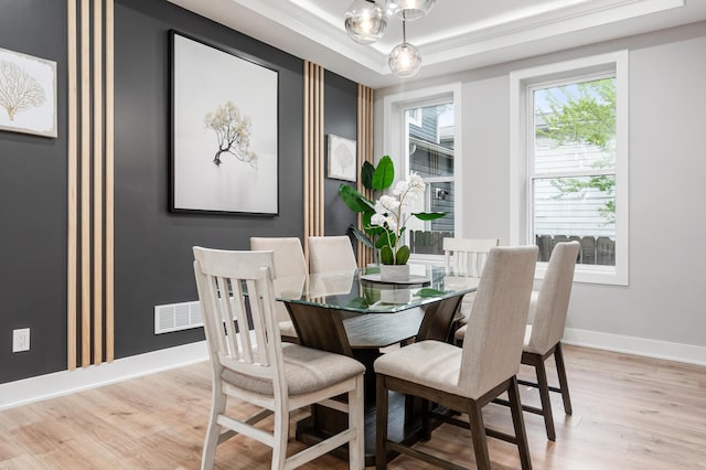 dining area with baseboards, light wood finished floors, a tray ceiling, and visible vents