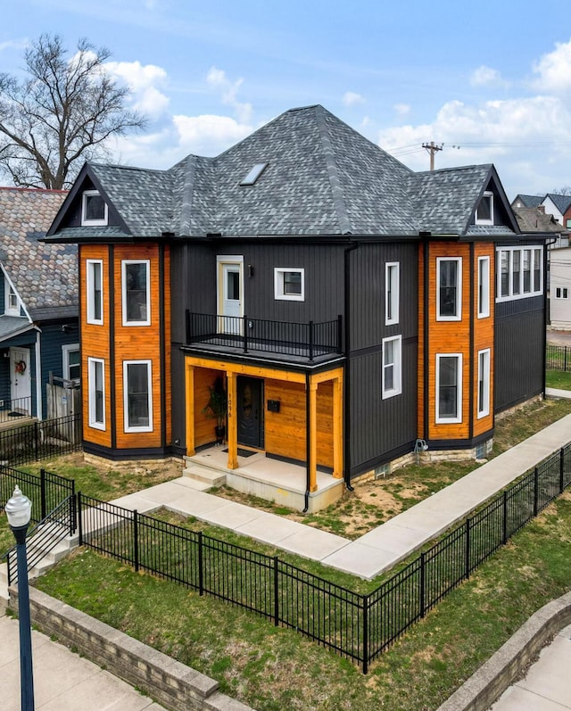 back of house with roof with shingles, a fenced front yard, a lawn, and a balcony