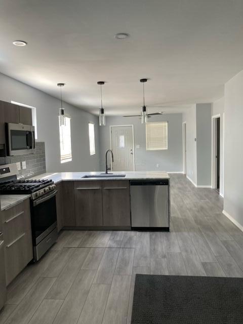 kitchen featuring a peninsula, light countertops, a sink, light wood finished floors, and appliances with stainless steel finishes