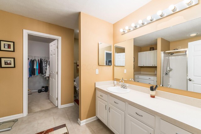 bathroom with tile patterned floors, baseboards, a spacious closet, a shower stall, and vanity