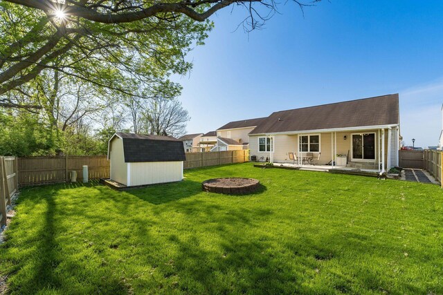 back of property featuring a fenced backyard, a shingled roof, a yard, a shed, and a patio