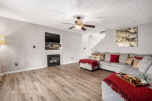 living room featuring baseboards, wood finished floors, ceiling fan, and a glass covered fireplace