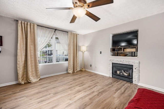 unfurnished living room with a fireplace, ceiling fan, baseboards, a textured ceiling, and wood finished floors
