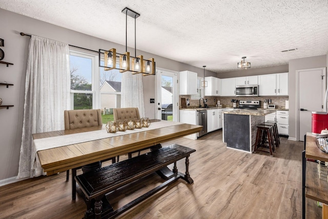dining room with a textured ceiling, a chandelier, light wood-type flooring, and visible vents