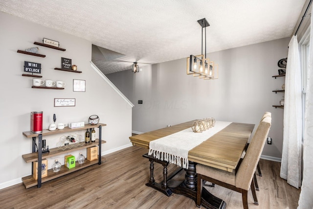 dining space featuring a textured ceiling, wood finished floors, and baseboards
