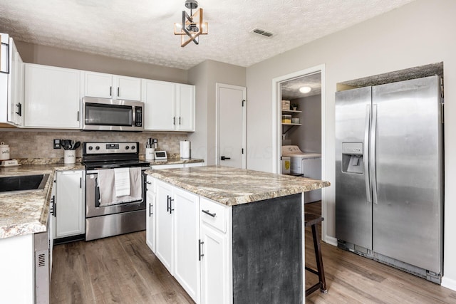 kitchen with backsplash, washing machine and clothes dryer, appliances with stainless steel finishes, and wood finished floors