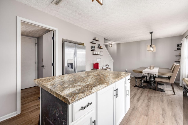 kitchen with stainless steel fridge with ice dispenser, white cabinets, a center island, light wood-type flooring, and a textured ceiling