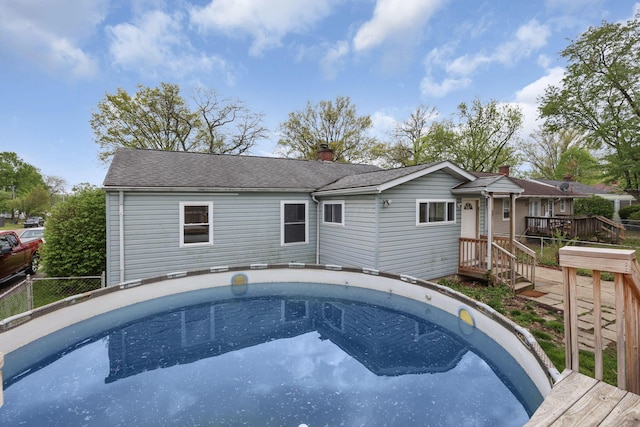 back of house with a fenced in pool, roof with shingles, fence, and a chimney