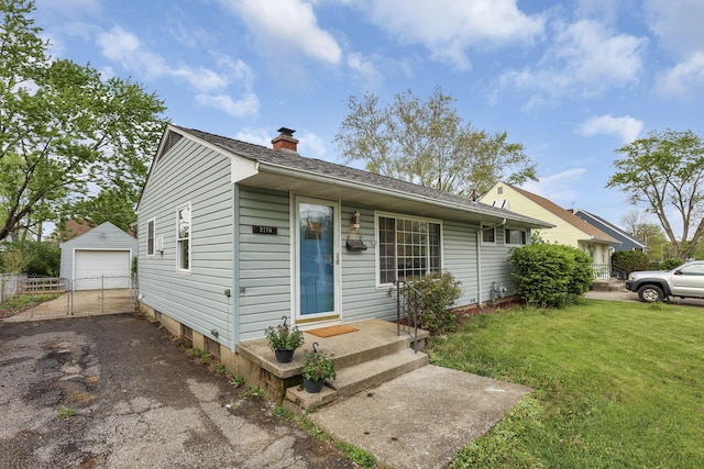 view of front facade featuring fence, aphalt driveway, a detached garage, a front yard, and an outdoor structure