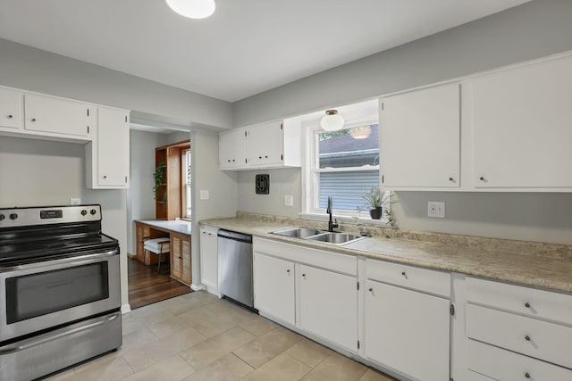 kitchen featuring appliances with stainless steel finishes, a sink, light tile patterned floors, light countertops, and white cabinetry