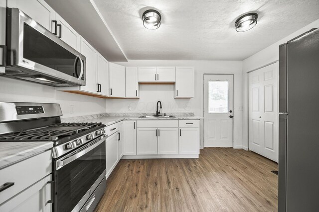 2728 Hiawatha St, Columbus, OH 43211 - kitchen with stainless steel appliances, a sink, wood finished floors, white cabinets, and a textured ceiling