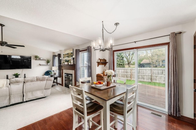 dining room featuring a glass covered fireplace, wood finished floors, visible vents, and ceiling fan with notable chandelier
