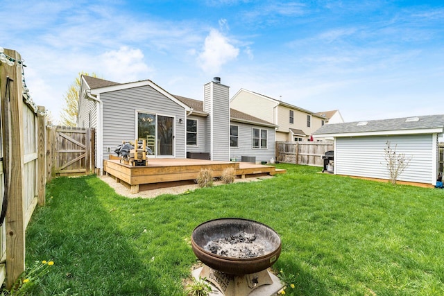 back of house featuring a gate, a fenced backyard, a yard, a wooden deck, and a fire pit