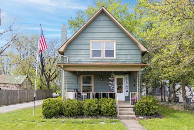 view of front of home featuring a porch, a front lawn, fence, and a chimney