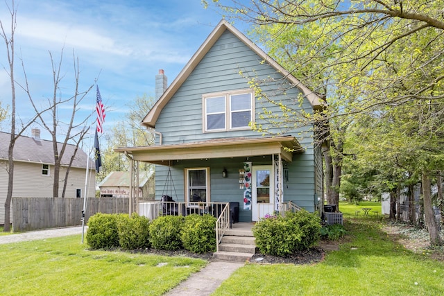 view of front of home with a porch, a chimney, fence, and a front yard