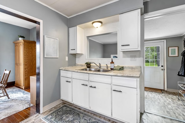 kitchen with a sink, light countertops, light wood-style floors, ornamental molding, and white cabinetry