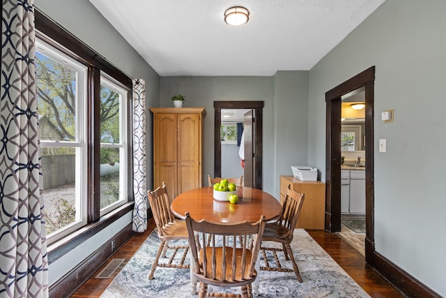 dining area with dark wood-style flooring, baseboards, visible vents, and plenty of natural light