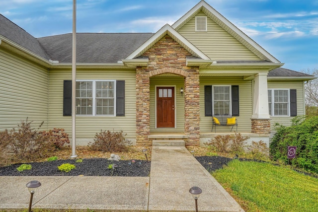 view of front of home with a porch, a shingled roof, and stone siding