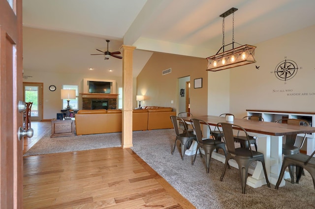 dining area with lofted ceiling, visible vents, a glass covered fireplace, light wood finished floors, and a ceiling fan
