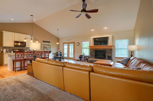 living room with high vaulted ceiling, a ceiling fan, and a stone fireplace