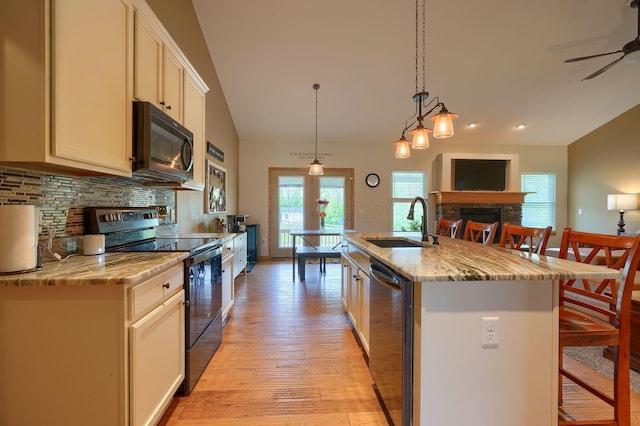 kitchen featuring tasteful backsplash, black appliances, a stone fireplace, a sink, and light wood-type flooring