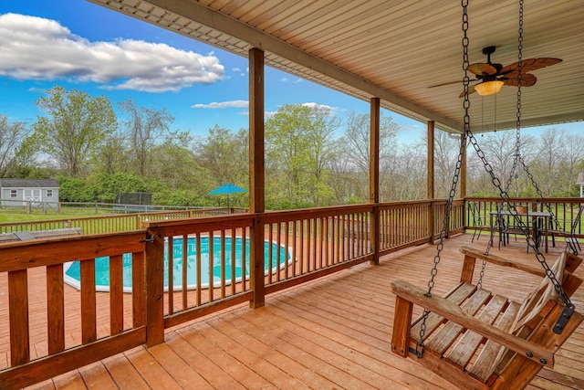 wooden terrace with a trampoline, ceiling fan, a fenced backyard, and a fenced in pool