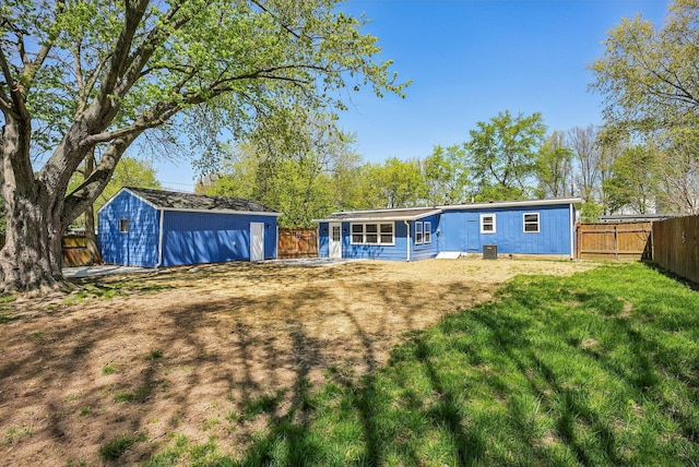rear view of property with an outdoor structure, central AC, a fenced backyard, a lawn, and a storage shed