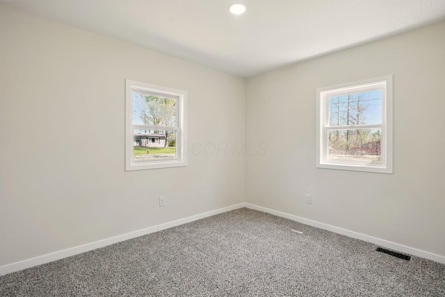 carpeted empty room featuring baseboards, plenty of natural light, and visible vents