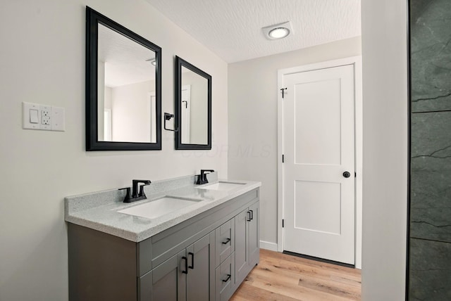 bathroom featuring a sink, a textured ceiling, double vanity, and wood finished floors