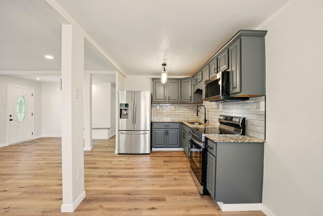 kitchen with a sink, light wood finished floors, backsplash, gray cabinetry, and stainless steel appliances