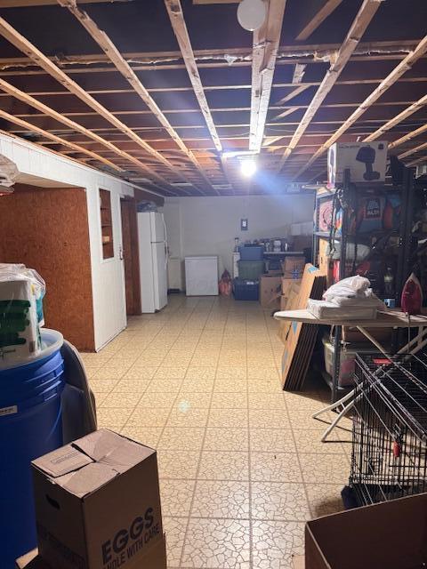 unfinished below grade area with tile patterned floors and freestanding refrigerator