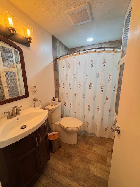 bathroom with toilet, vanity, a textured ceiling, and curtained shower