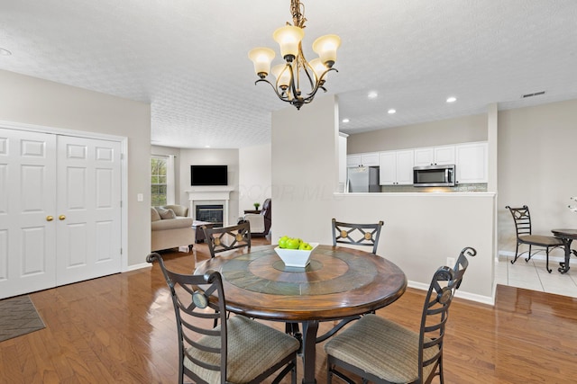 dining area with an inviting chandelier, visible vents, wood finished floors, baseboards, and a glass covered fireplace